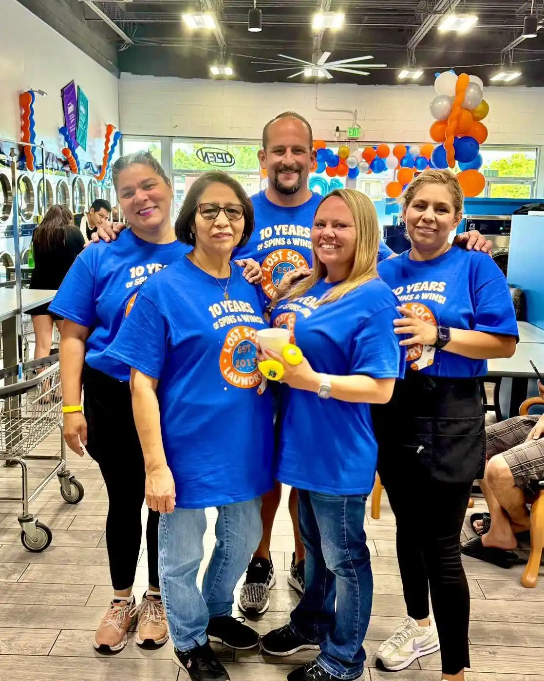 The Lost Sock Laundry team poses together inside their clean, modern West Valley City laundromat, showcasing the friendly staff dedicated to providing self-service laundry, Wash Dry Fold service, oversized washer access, and exceptional customer care for local families.
